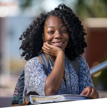 Student standing, smiling and wearing a backpack in front of a blurred background